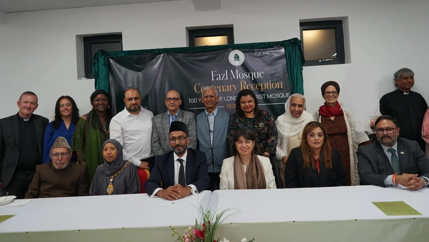 Two rows of guests, seated and standing, behind a long white table in front of a banner reading Fazl Mosque Centenary Reception, 100 years of London's first mosque
